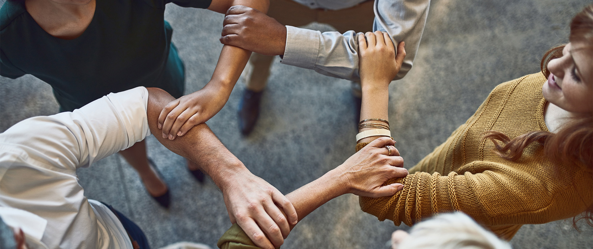 Ein Team von vier Personen bildet mit ihren Armen einen runden Kreis und symbolisiert Zusammenhalt. Teamwork, Teamentwicklung, Personalentwicklung, Persönlichkeitsanalyse, Team Management Systems, Team Management Profil, TMP, TMS, Team Management Services GmbH